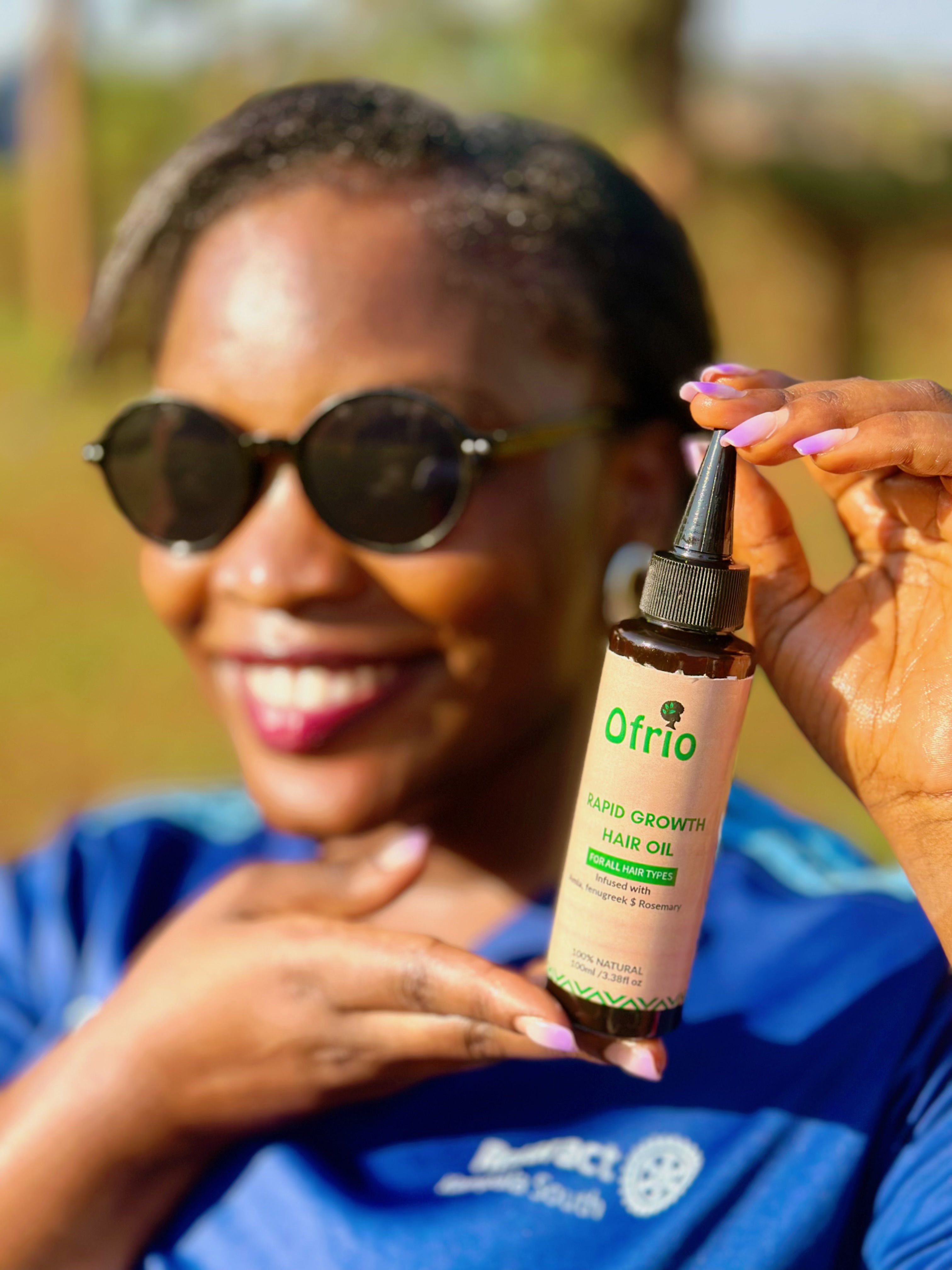 Ofrio Rapid Growth Hair Oil held against a warm outdoor background